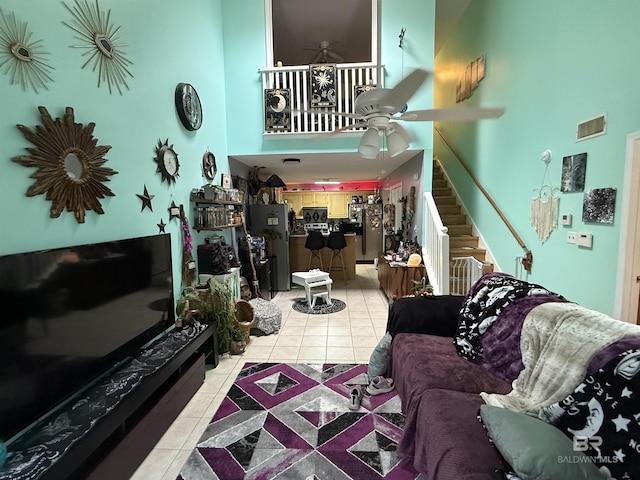 living room featuring light tile patterned flooring, a high ceiling, visible vents, a ceiling fan, and stairway