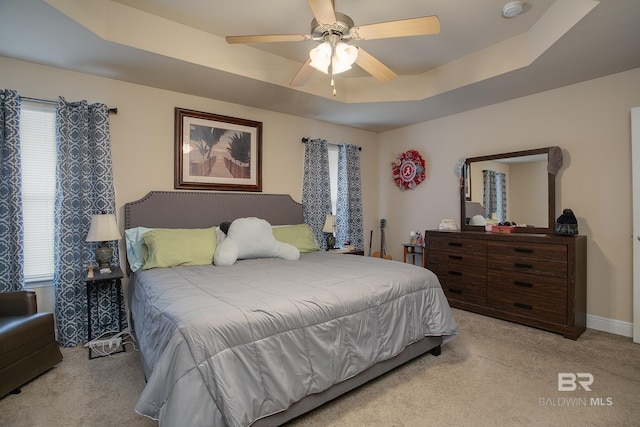 bedroom with ceiling fan, light colored carpet, and a raised ceiling