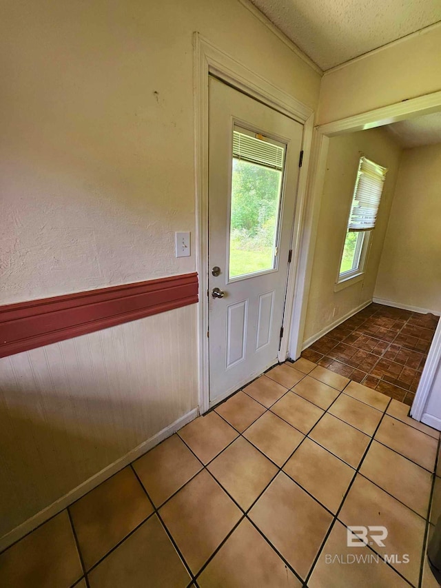 doorway featuring tile patterned floors, a textured ceiling, and wainscoting