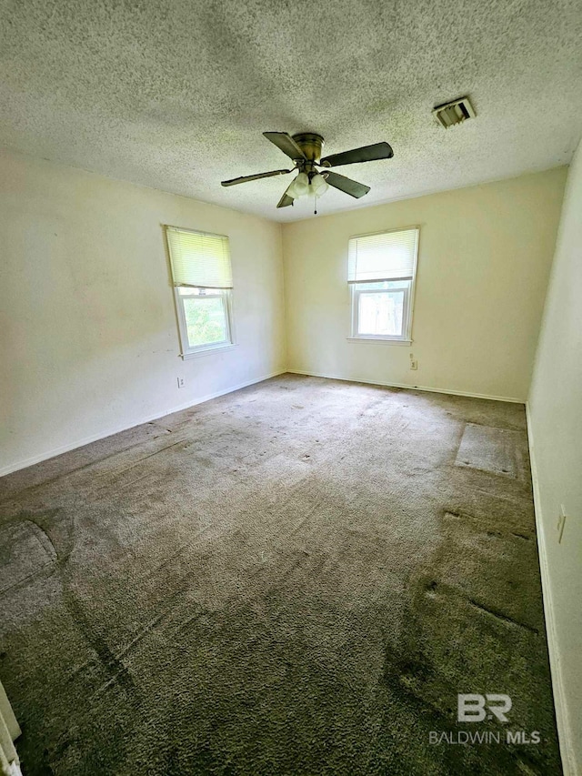 carpeted empty room featuring visible vents, baseboards, a textured ceiling, and ceiling fan