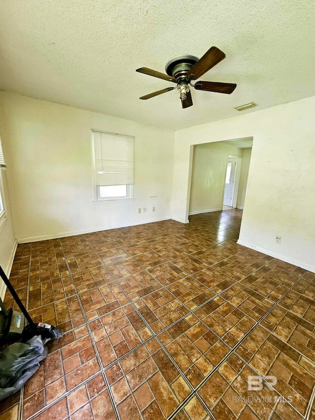 empty room with visible vents, baseboards, ceiling fan, tile patterned floors, and a textured ceiling