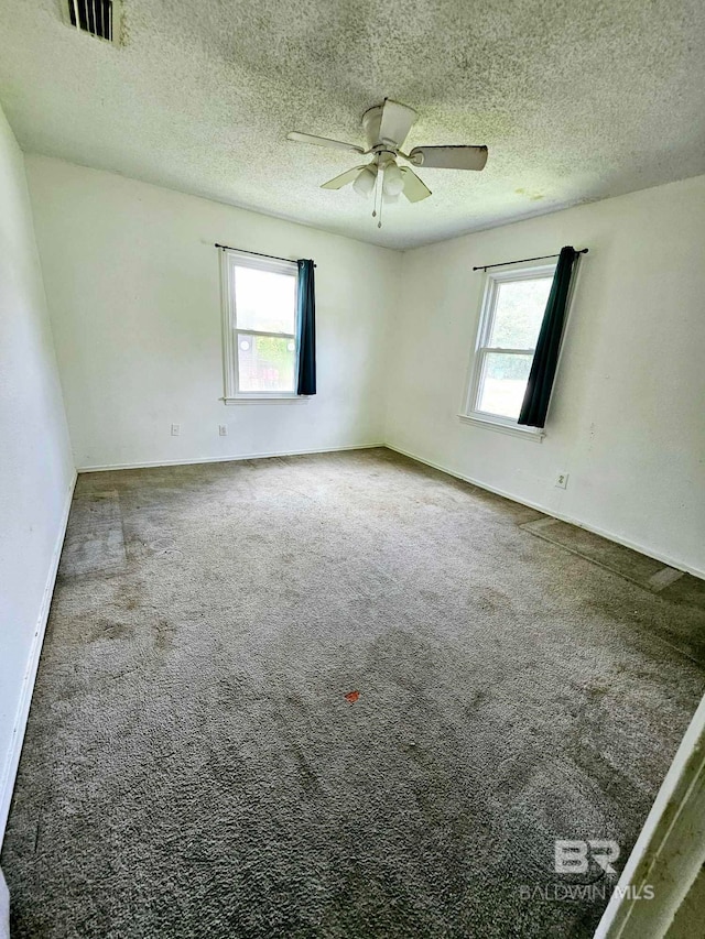 carpeted spare room with a wealth of natural light, visible vents, a textured ceiling, and ceiling fan