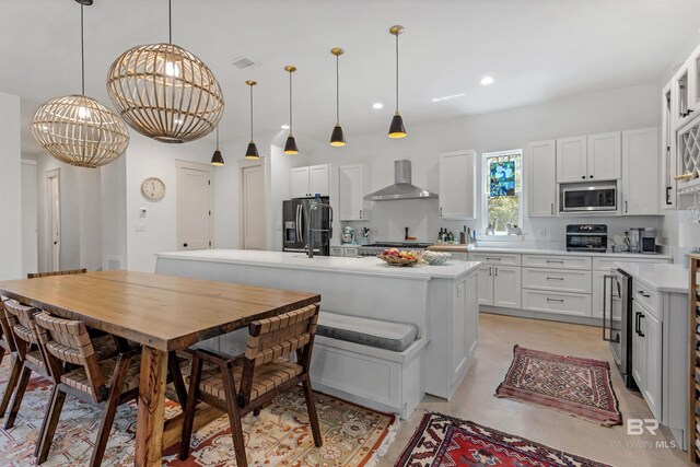 kitchen featuring a center island, hanging light fixtures, stainless steel appliances, and wall chimney exhaust hood