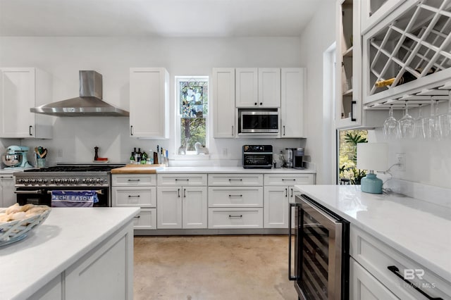 kitchen with stainless steel microwave, wall chimney range hood, white cabinets, beverage cooler, and range with two ovens