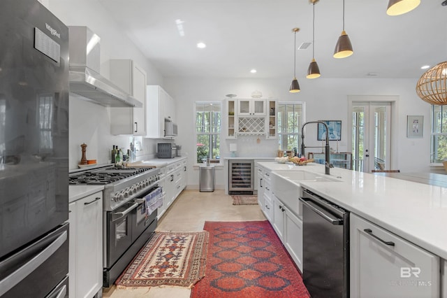 kitchen with wall chimney range hood, beverage cooler, white cabinets, dishwasher, and double oven range