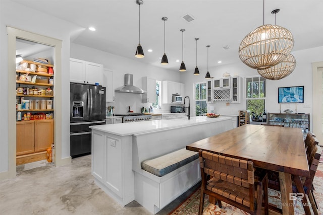 kitchen featuring wall chimney range hood, white cabinetry, black fridge with ice dispenser, and hanging light fixtures