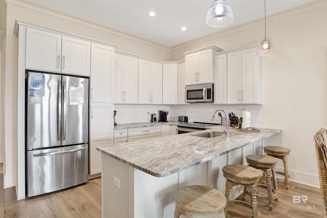 kitchen featuring stainless steel appliances, a peninsula, light stone counters, white cabinets, and a breakfast bar area