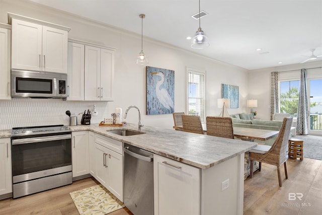 kitchen featuring stainless steel appliances, a sink, a peninsula, light wood-type flooring, and open floor plan