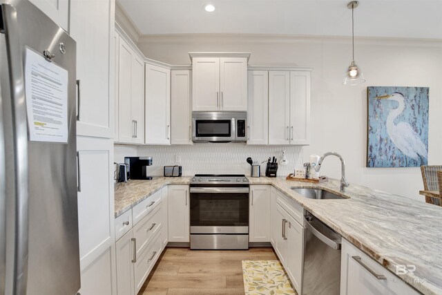 kitchen with appliances with stainless steel finishes, a sink, crown molding, white cabinets, and light wood-type flooring
