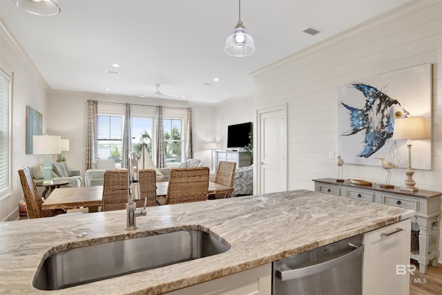 kitchen featuring stainless steel dishwasher, open floor plan, a sink, light stone counters, and crown molding