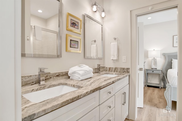 ensuite bathroom featuring a stall shower, double vanity, wood finished floors, and recessed lighting