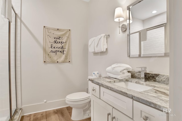 bathroom featuring a stall shower, wood finished floors, toilet, vanity, and baseboards