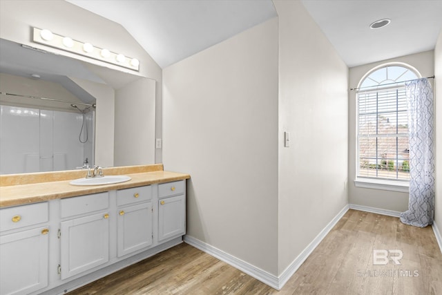 bathroom with hardwood / wood-style flooring, vaulted ceiling, walk in shower, and vanity