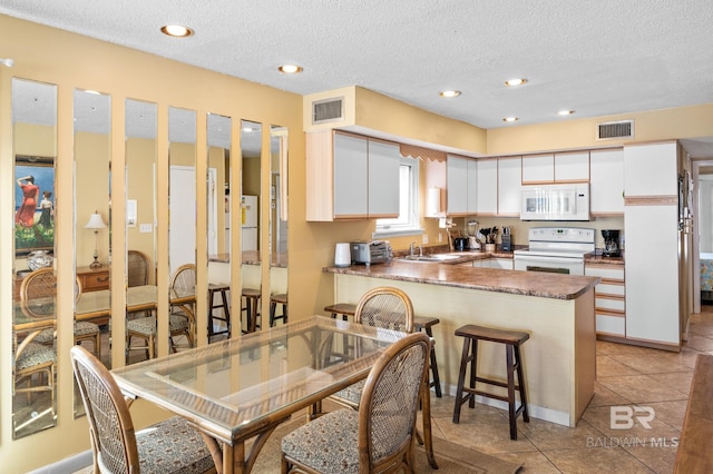 kitchen with a breakfast bar area, light tile patterned floors, kitchen peninsula, white appliances, and white cabinets