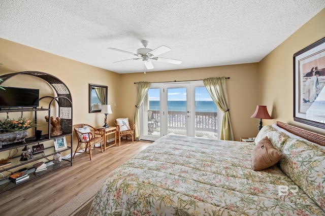 bedroom with a water view, a textured ceiling, light wood-type flooring, ceiling fan, and access to exterior