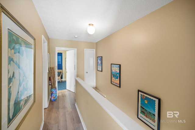 corridor with a textured ceiling and light hardwood / wood-style flooring