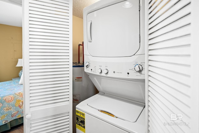 clothes washing area featuring stacked washer and dryer, water heater, and a textured ceiling