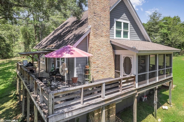 rear view of house featuring a wooden deck, a sunroom, and a yard