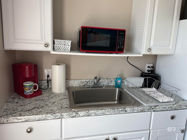 kitchen featuring light stone counters, sink, and white cabinets