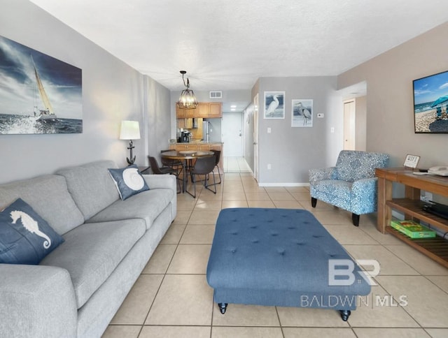 living area with visible vents, a textured ceiling, an inviting chandelier, light tile patterned flooring, and baseboards