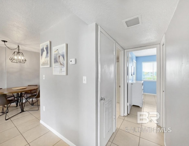 hall featuring light tile patterned flooring, baseboards, a chandelier, and a textured ceiling