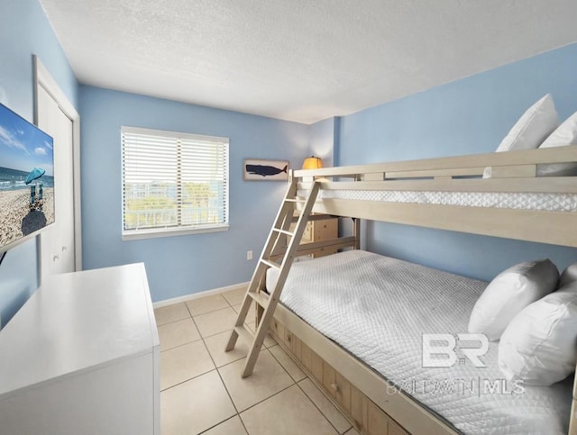 bedroom featuring light tile patterned floors, baseboards, and a textured ceiling