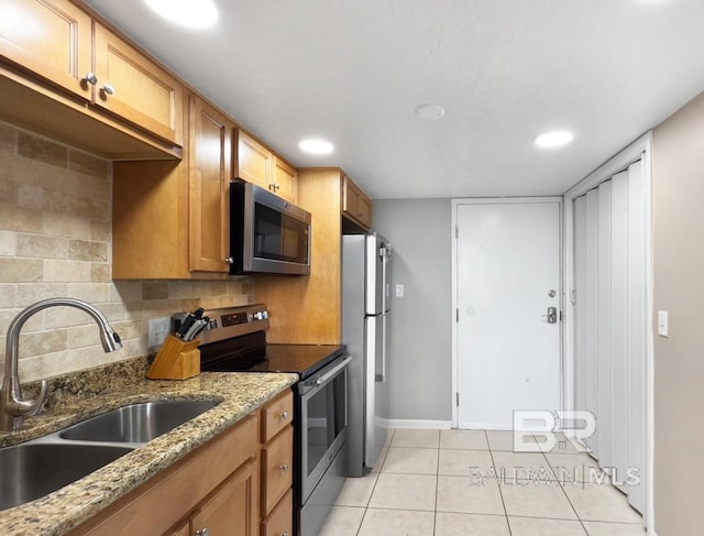 kitchen featuring light tile patterned floors, light stone countertops, a sink, stainless steel appliances, and tasteful backsplash