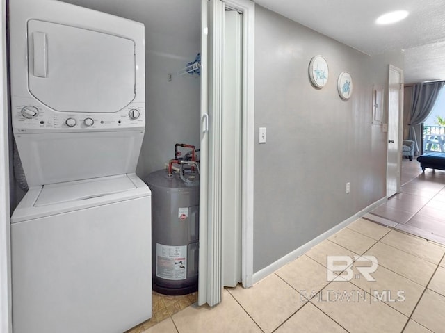 washroom featuring stacked washer / dryer, light tile patterned floors, baseboards, and water heater