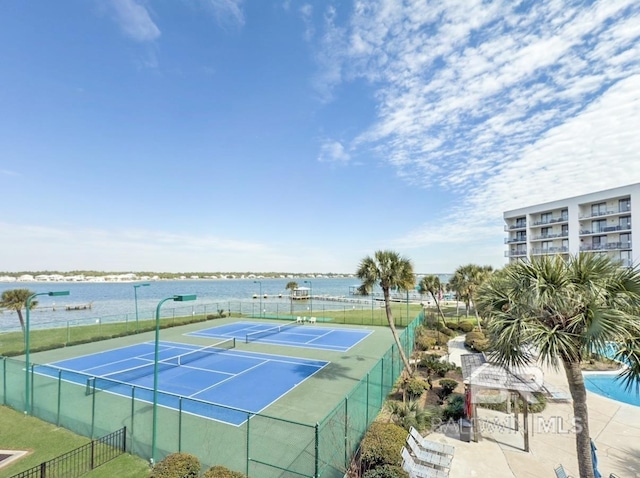 view of tennis court featuring fence and a water view