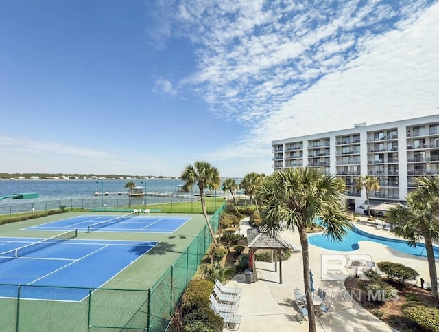 view of tennis court featuring a water view and fence