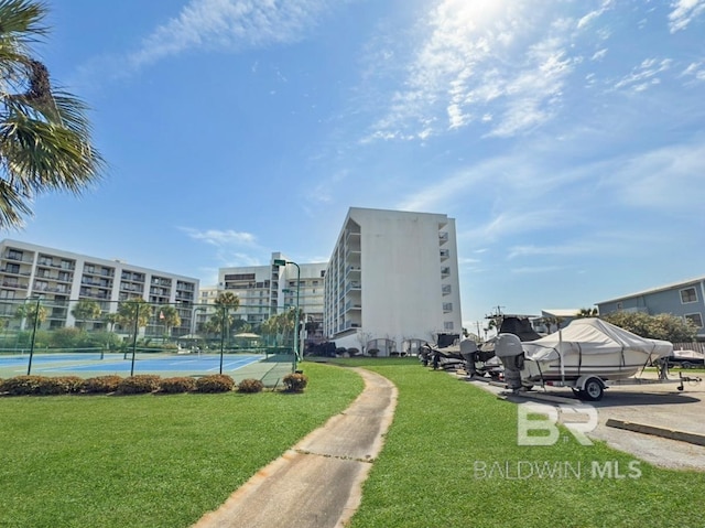 view of property's community featuring a tennis court, a lawn, and fence