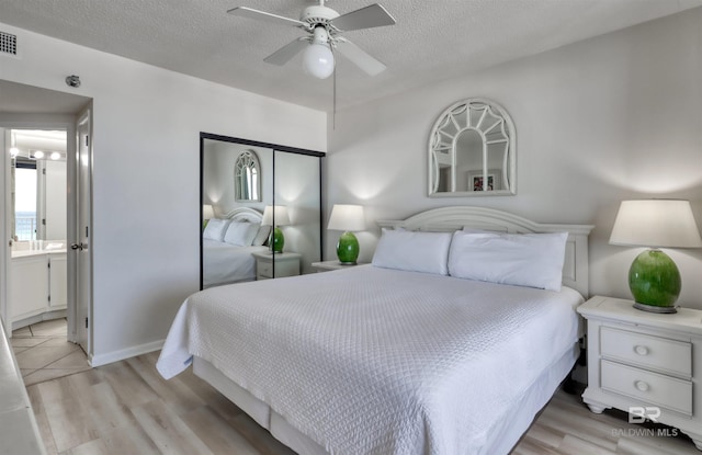 24770 Perdido Beach Blvd Unit 402, Orange Beach, AL 36561 - bedroom with light wood-style flooring, a textured ceiling, ensuite bath, and a ceiling fan