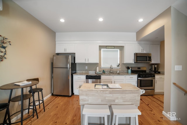 kitchen with white cabinets, a sink, appliances with stainless steel finishes, and light wood-style flooring