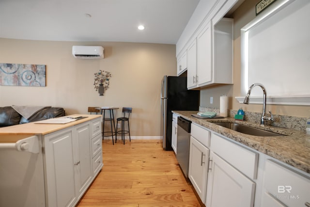 kitchen featuring white cabinetry, a wall mounted AC, stainless steel dishwasher, a sink, and light wood-style floors