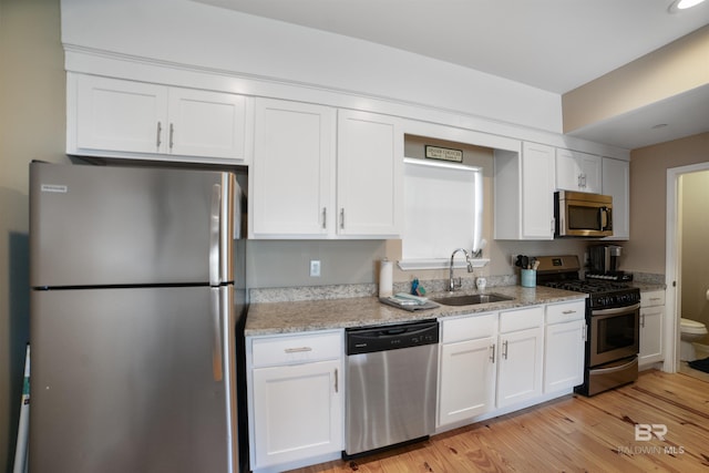 kitchen with light stone counters, a sink, white cabinetry, appliances with stainless steel finishes, and light wood-type flooring