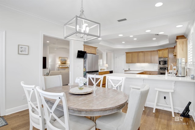 dining area featuring a tray ceiling, visible vents, light wood-type flooring, and crown molding