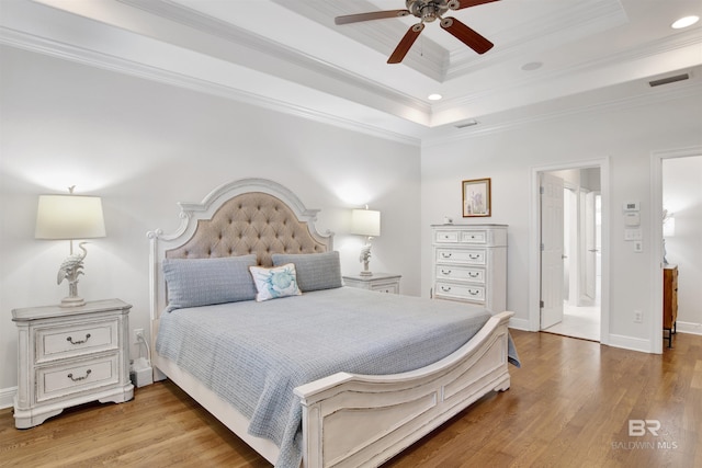bedroom with crown molding, a tray ceiling, wood finished floors, and visible vents