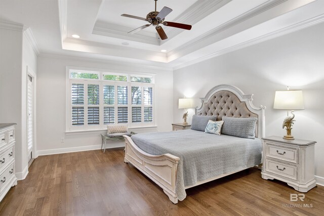 bedroom featuring baseboards, a raised ceiling, a ceiling fan, crown molding, and wood finished floors