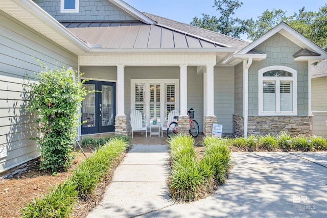 entrance to property with french doors, stone siding, covered porch, and roof with shingles