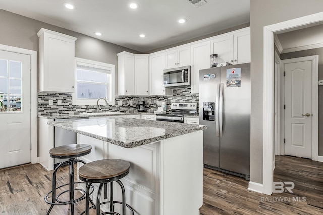 kitchen featuring white cabinetry, appliances with stainless steel finishes, light stone counters, and a kitchen island