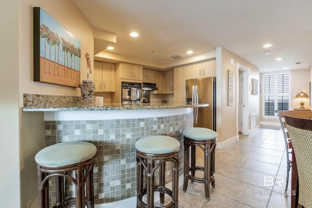 kitchen with light stone counters, light tile patterned floors, light brown cabinetry, under cabinet range hood, and stainless steel fridge with ice dispenser