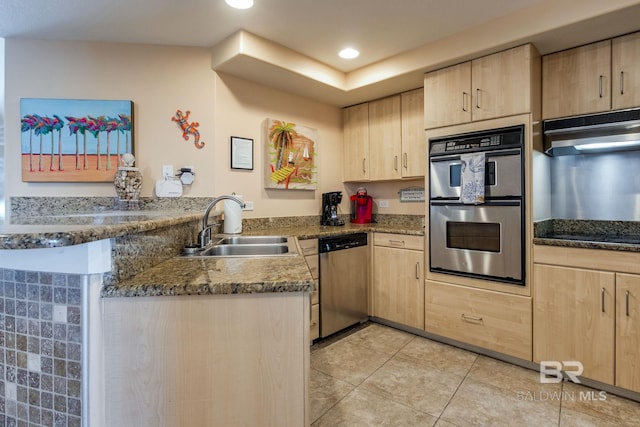 kitchen featuring a peninsula, light brown cabinets, stainless steel appliances, and a sink