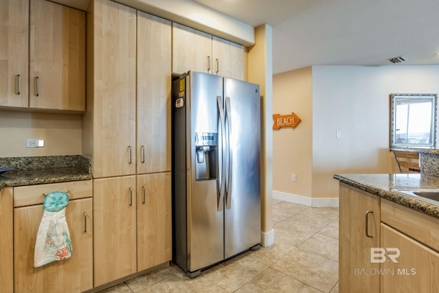 kitchen with light tile patterned floors, light brown cabinets, visible vents, stainless steel refrigerator with ice dispenser, and dark stone counters