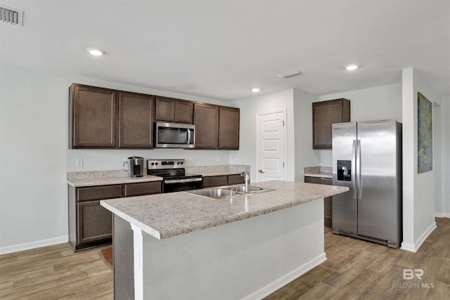 kitchen featuring sink, a kitchen island with sink, dark brown cabinets, stainless steel appliances, and light wood-type flooring