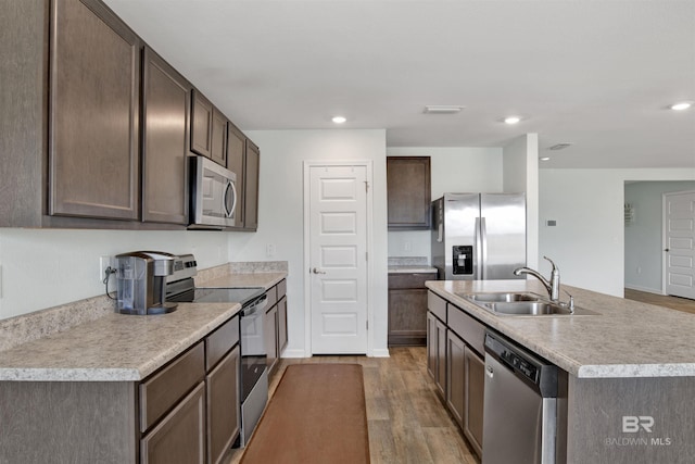 kitchen with dark brown cabinetry, sink, an island with sink, stainless steel appliances, and light hardwood / wood-style floors