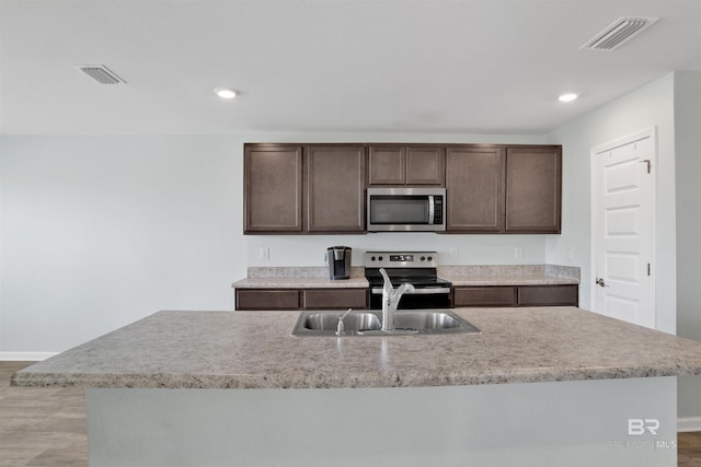 kitchen with appliances with stainless steel finishes, sink, a center island with sink, and dark brown cabinets