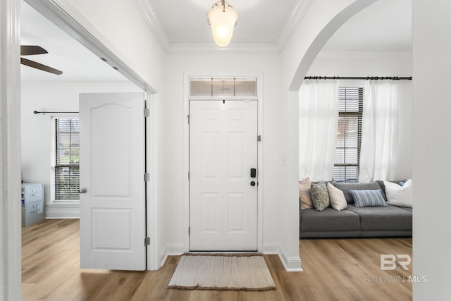 entryway featuring arched walkways, crown molding, and light wood-style floors