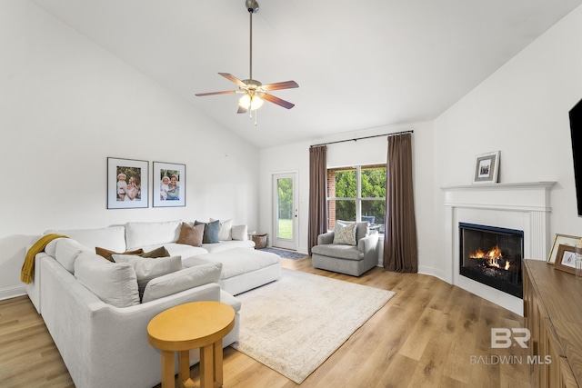 living area with light wood-style flooring, a warm lit fireplace, high vaulted ceiling, and a ceiling fan