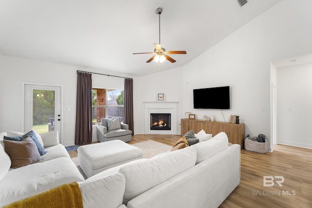 living room featuring a lit fireplace, baseboards, light wood finished floors, and ceiling fan