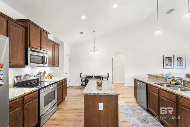 kitchen with a sink, a center island, arched walkways, appliances with stainless steel finishes, and vaulted ceiling